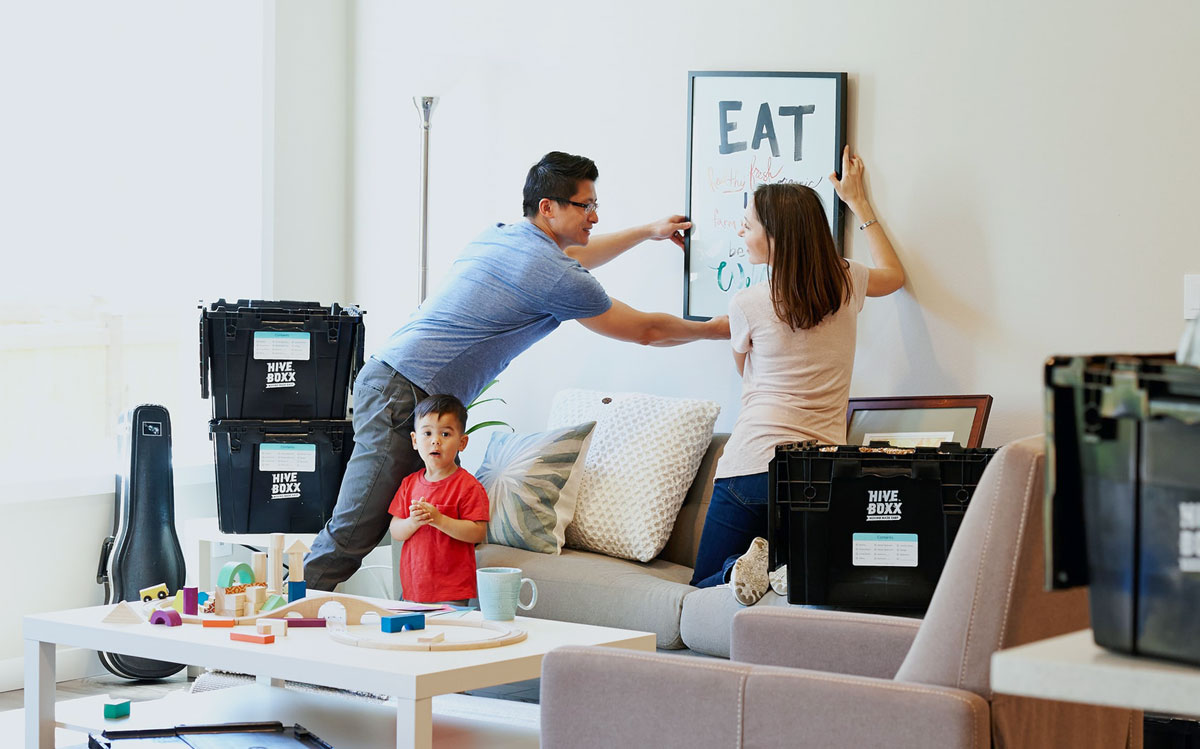 Couple hanging a photo on the wall after moving into their rental home with their small son standing next to them and looking at the photographer