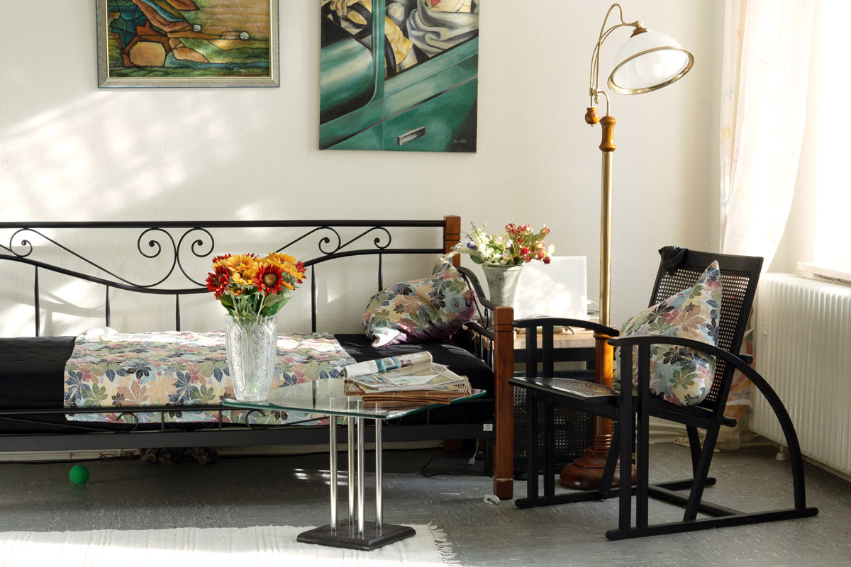 Couch with metal frame placed underneath two paintings hanging on the wall and next to a floor lamp and a black chair