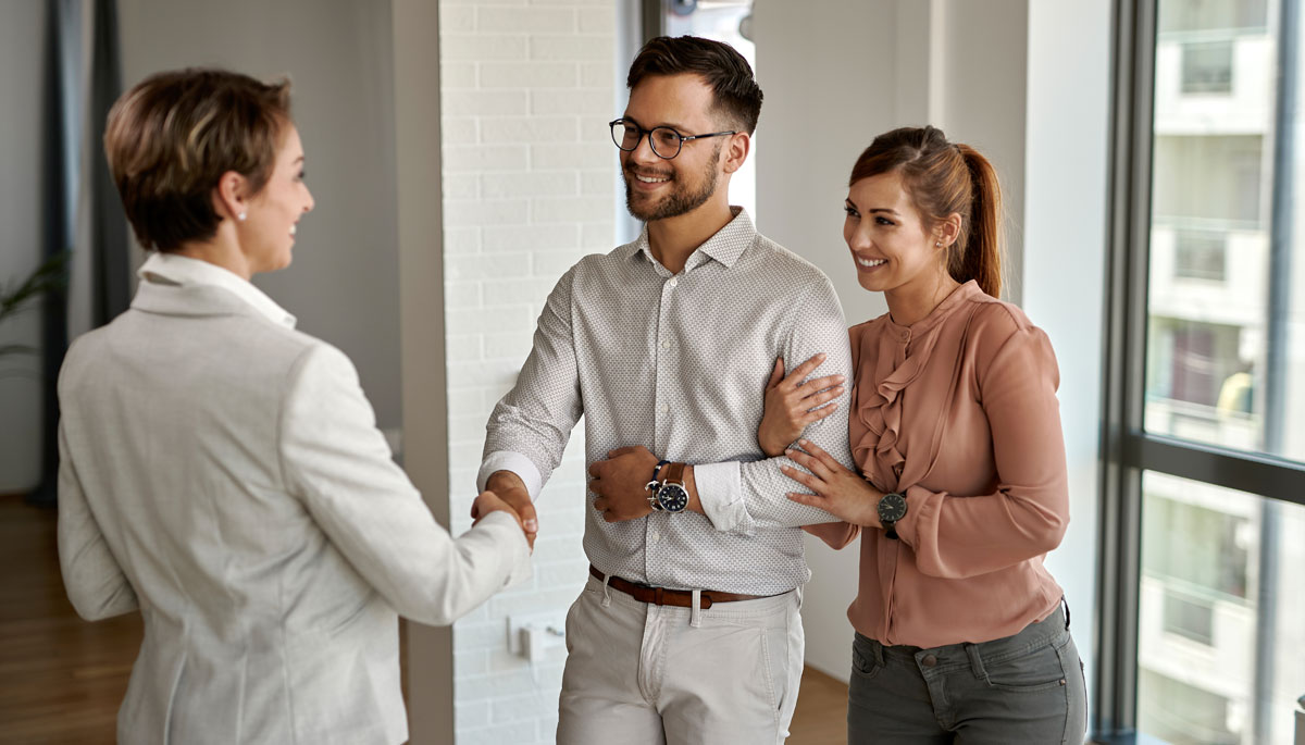 Young happy couple shaking hands with real estate agent