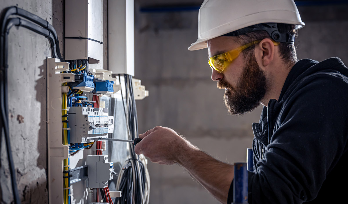 An electrician works in a switchboard with an electrical connecting cable