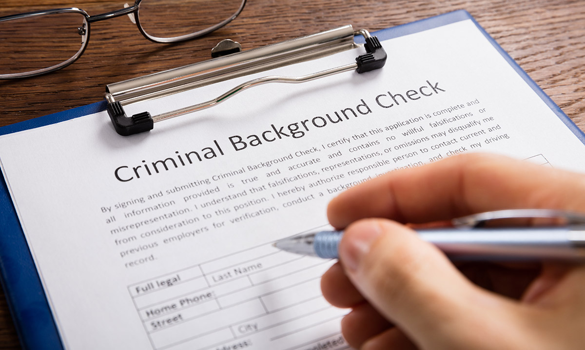 Close-up Of Person Hand Filling Criminal Background Check Application Form