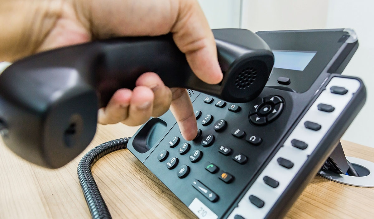 Male hand holding telephone receiver while dialing a telephone number to make a call