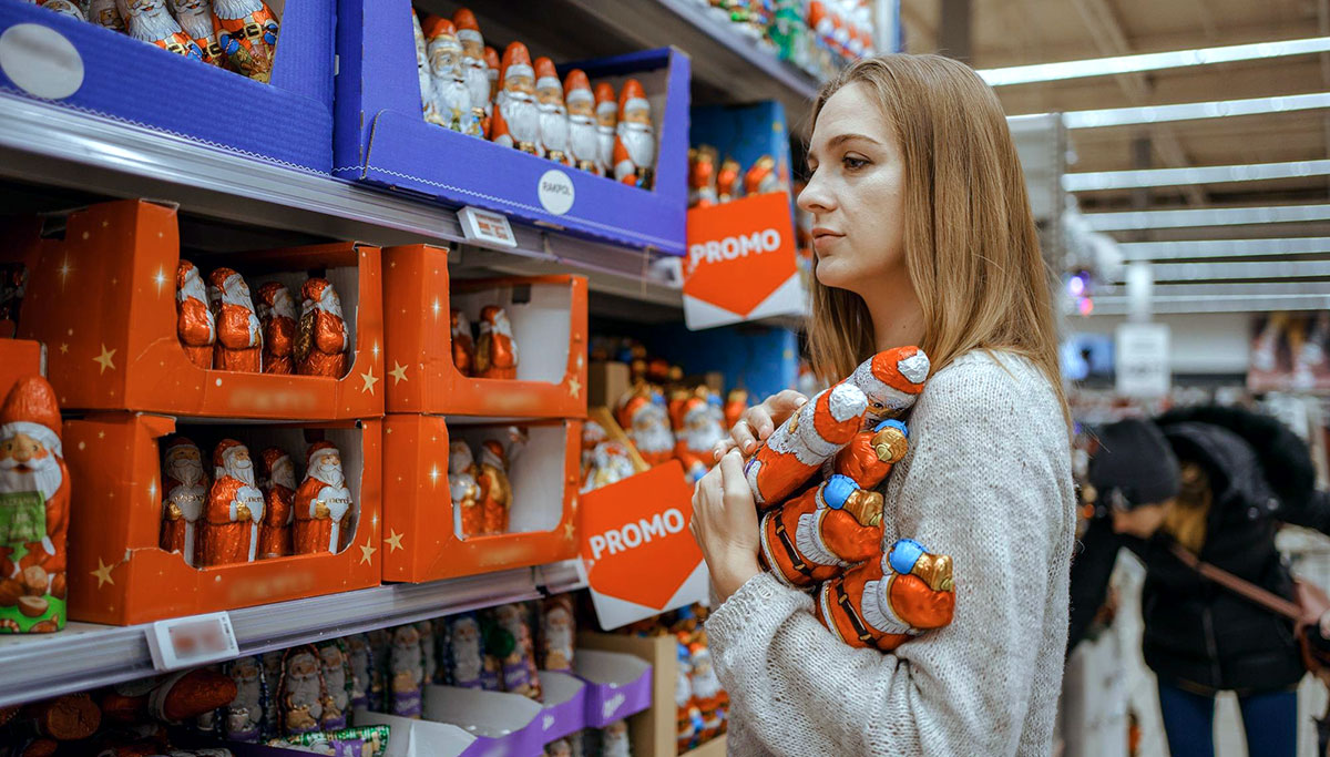 A young woman chooses a gift set for Christmas to a child on a supermarket shelf