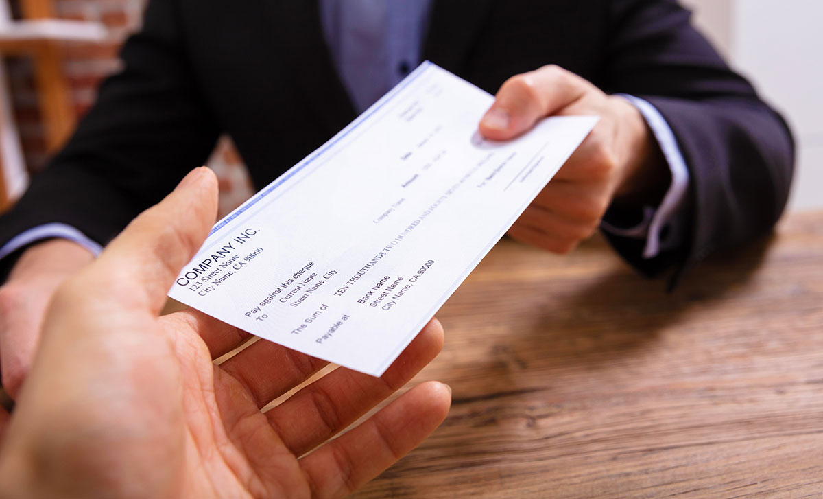 Man's Hands Giving Cheque To Other Person