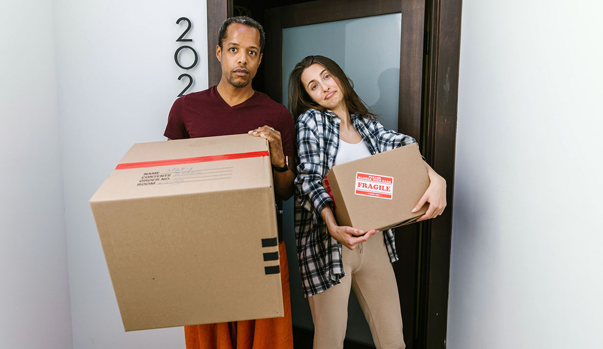 Two people standing by the door while holding cardboard boxes