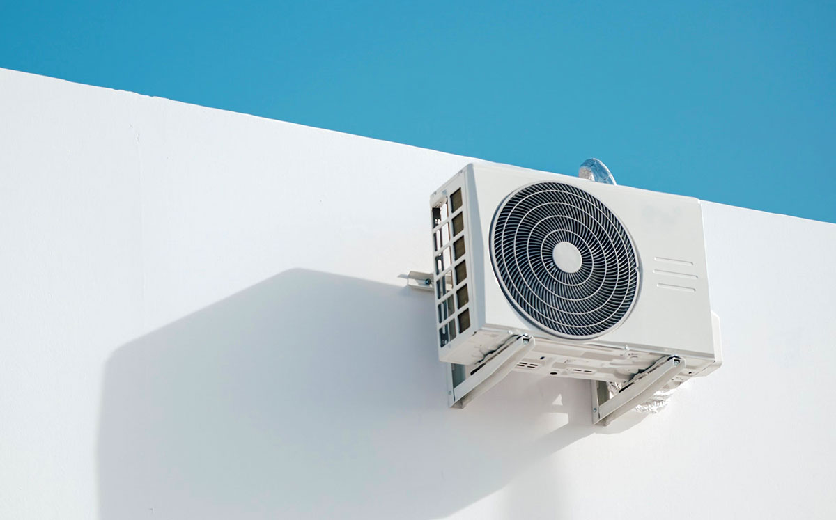 Wall-mounted air conditioner unit on a white building, set against a clear blue sky, creating a minimalist aesthetic